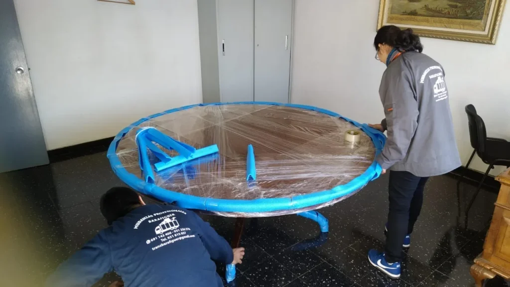 Operarios de Mudanzas Barafiguer protegiendo una mesa redonda con film antes de la mudanza