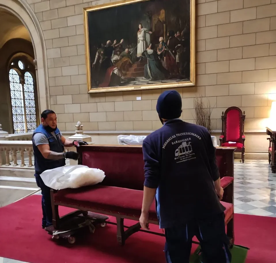 Operarios protegiendo un banco tapizado en una sala histórica antes de trasladarlo