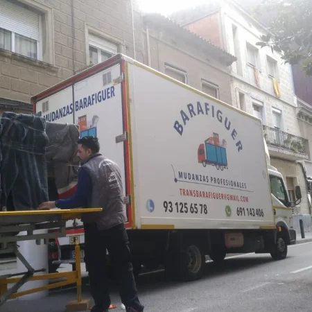 Operario cargando muebles envueltos en mantas en la plataforma elevadora junto al camión