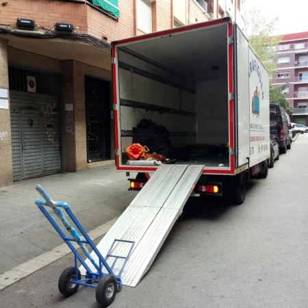 Camión de mudanzas con la rampa desplegada y una carretilla en una calle de Barcelona