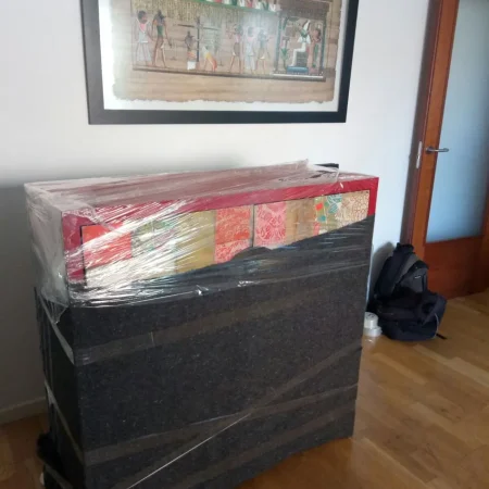 Muebles envueltos en film y manta apilados bajo un cuadro enmarcado en una vivienda