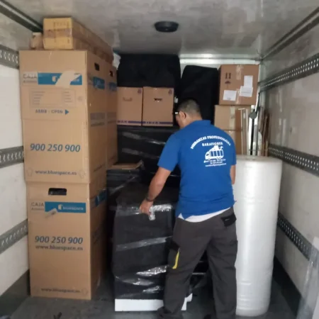 Operario cargando muebles protegidos y cajas dentro del camión de mudanzas