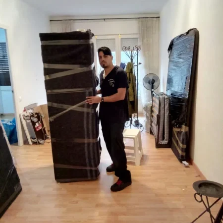 Operario moviendo un mueble alto protegido con manta en el salón de una vivienda