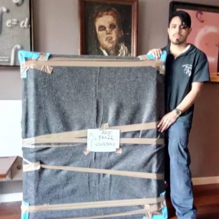 Operarios sujetando un cuadro embalado en un bastidor de madera con la etiqueta de frágil
