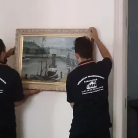Dos operarios de Mudanzas Barafiguer descolgando un cuadro enmarcado en una vivienda de Barcelona