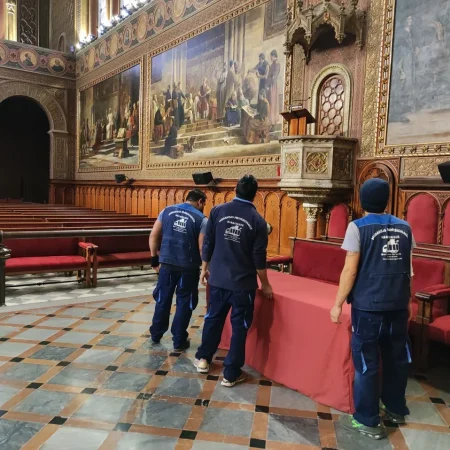 Operarios trasladando un banco tapizado en una sala histórica con murales