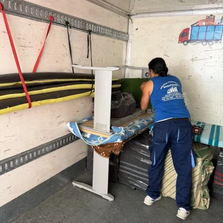 Operario asegurando con cinchas los muebles protegidos dentro del camión de mudanzas